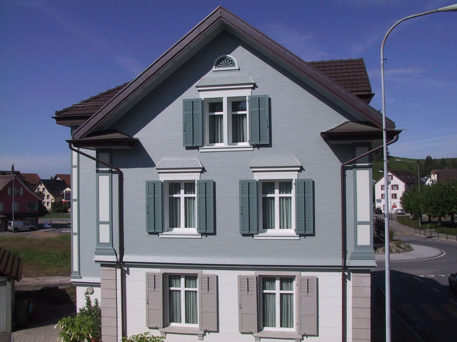 Sanierte Fassade mit Schindelschirm und grünen Fensterläden