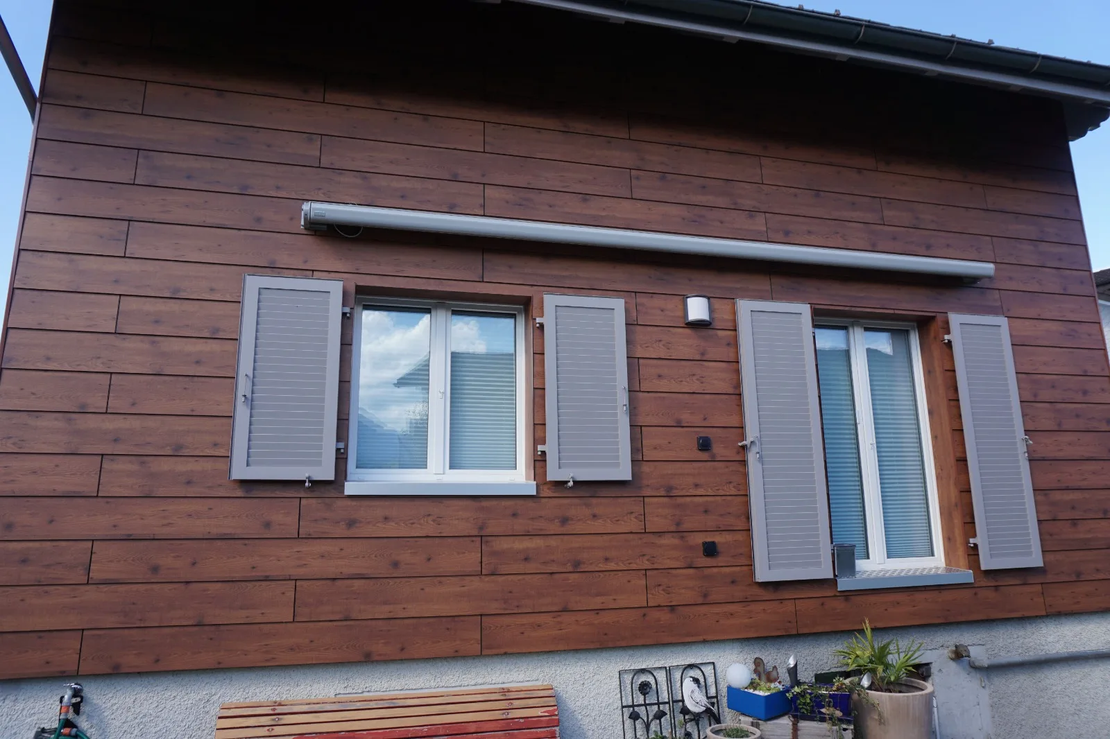 Fassade in Holzoptik mit grauen Fensterläden und Markise